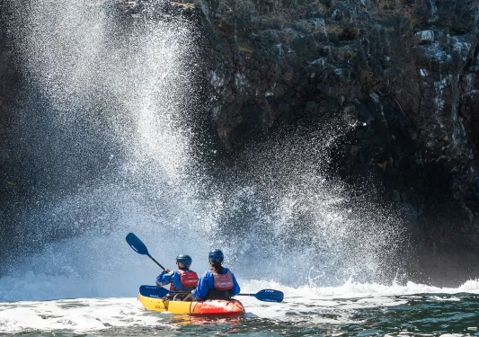 Two people paddling on a kayak in front of an active waterfall