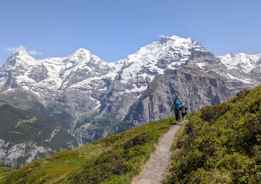 Mom and son hiking on a gravel trail with snow-capped mountains in the background