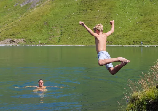 Boy jumping into a lake with his dad swimming in the water
