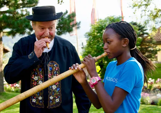Girl blowing into a long instrument with a man blowing into a smaller instrument
