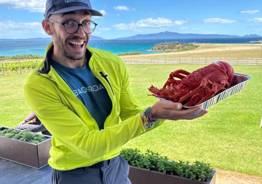 Man wearing a yellow jacket, holding up a tray with a boiled lobster