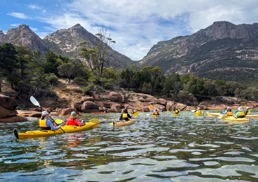 Group of people paddling in individual, yellow kayaks in a lake