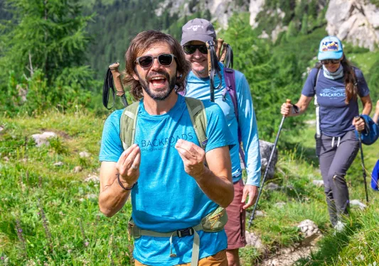 Two men and one woman walking on a trail with grassy hills in the background