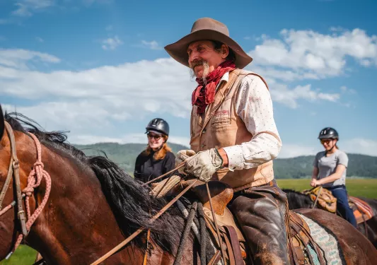 Man with cowboy gear and a long beard horseback riding
