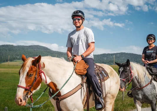Man wearing sunglasses and a helmet, riding on the back of a horse