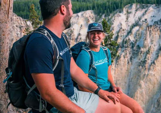 Man and woman sitting on a cliff, with large cliffs in the distance