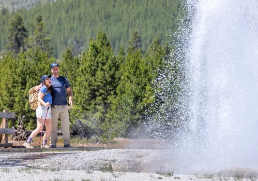 Man and woman smiling while standing in front of an active geyser