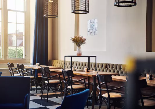 Cafe with cushioned sofas and black chairs around square tables