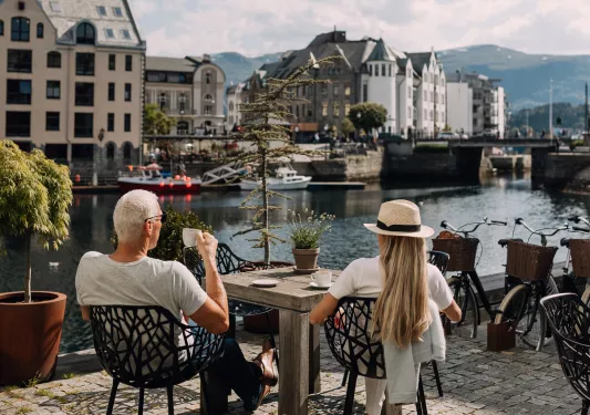 Man and woman sitting on a stone patio, drinking coffee and looking out to a river