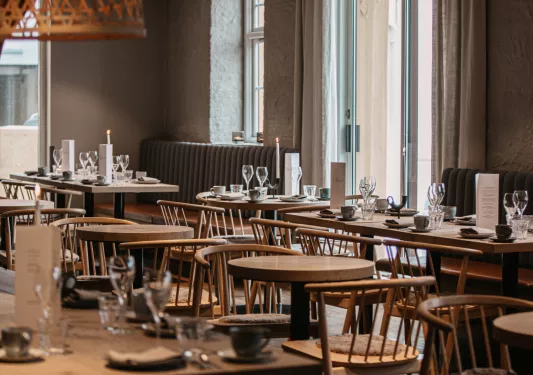 Dining hall with wooden tables and chairs, with wine glasses on each table