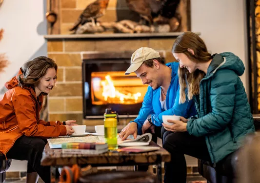 Man and two women sitting by a table in front of a fireplace, looking at a large map