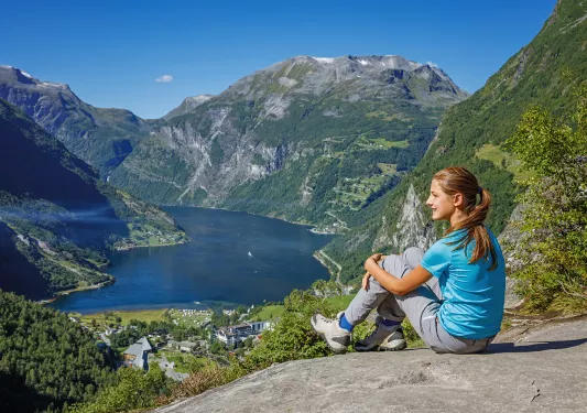 Woman sitting on a boulder, looking out to large mountains and a lake