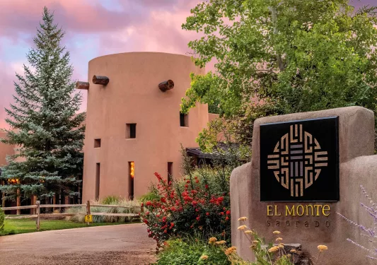 Exterior view of a clay hotel building with a stone "El Monte" sign