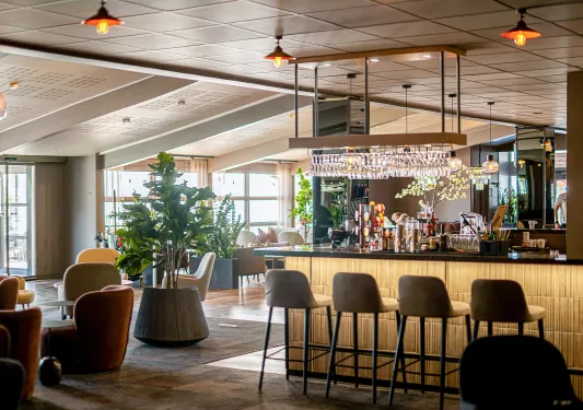 Bar and lounge with cushioned stools and chairs, with a bar counter to the right