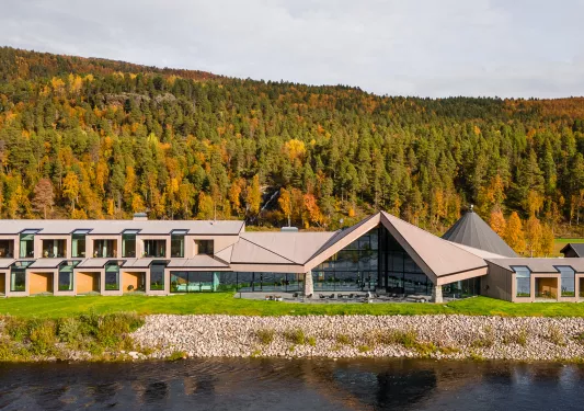 Long hotel complex with large glass walls and a forest in the background