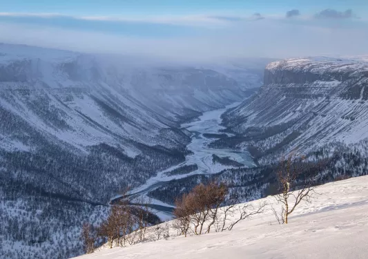 Large, open valley of snowy mountains with a river in the center