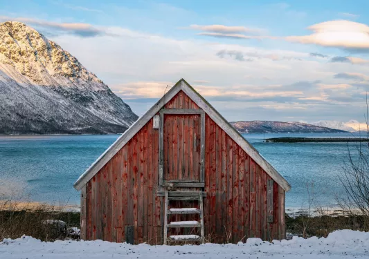 Red shed in a valley of snow with the ocean in the background