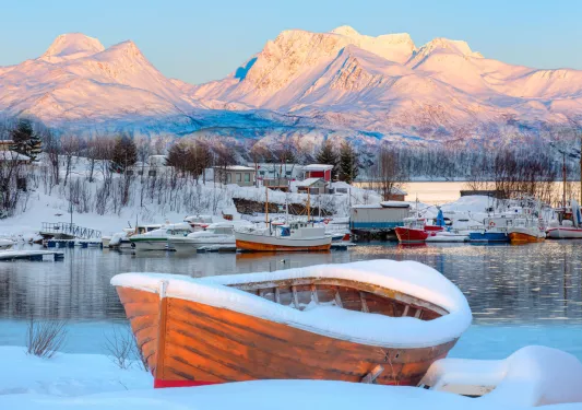 Wooden boats surrounding a lake, covered in snow with snowy mountains in the distance