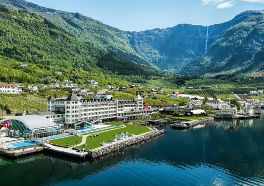 Exterior, wide view of a white hotel complex in front of a port with boats in front