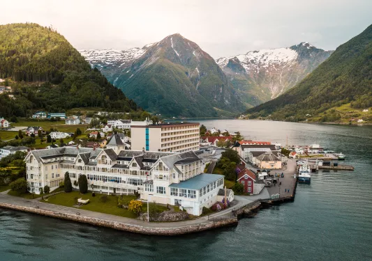 Exterior, sky view of a hotel complex with a lake in front and mountains in the background