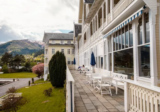 Hotel building with an outdoor patio with white tables and chairs, with a grass area to the left