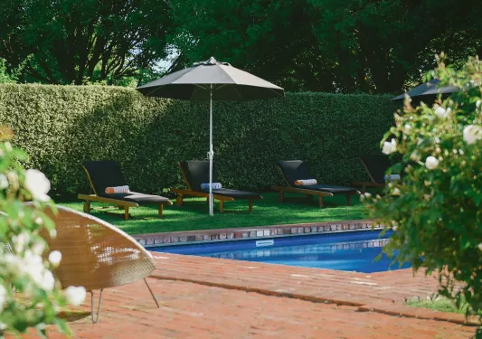 Outdoor pool surrounded by wooden chairs and trimmed hedges