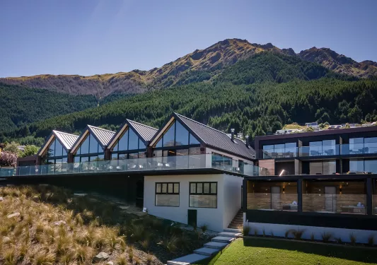 Exterior view of  a row of buildings with glass walls, and tall mountains in the background