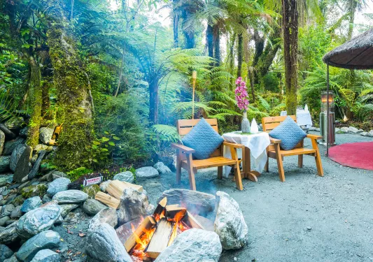 Outdoor camping area with a stone fireplace and two wooden chairs