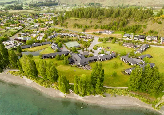 Sky view of hotel complex buildings in the middle of a valley with a small town and tall trees in the background