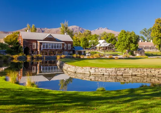 Large grass area with a small pond and a wooden building in the background