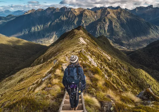 Woman descending a mountain with large mountains in the background