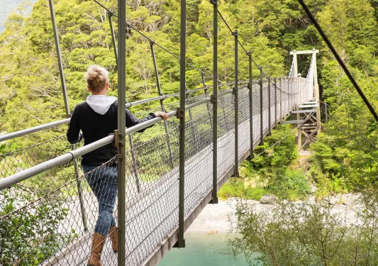 Woman walking on a wooden, suspended bridge with a river underneath