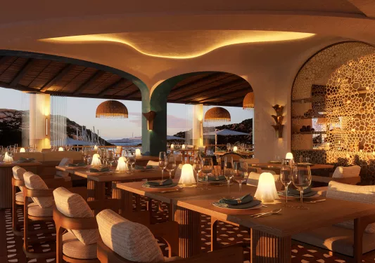 Outdoor patio with dining tables and wine glasses on each table, with cliffs and the ocean in the distance