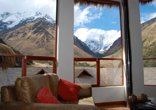 Corner room with large windows and a cushioned chair, looking out towards tall mountains