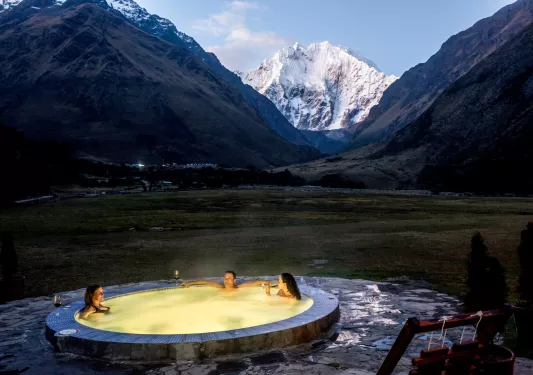 Outdoor hot tub with an illuminated yellow light, with snow capped mountains in the background
