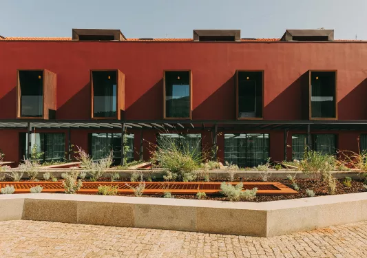 Exterior view of a red building with large windows and a small plant enclosure in front