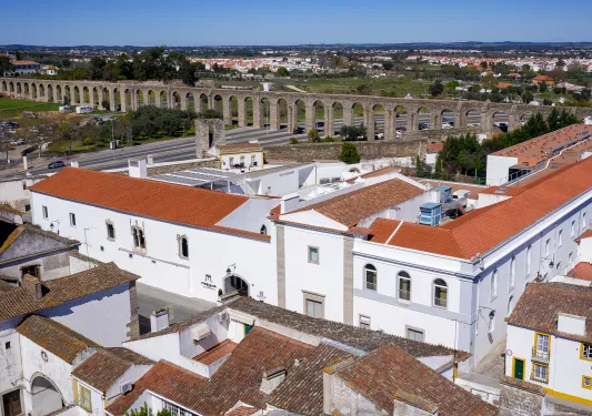 Exterior view of a large white building with red roofing, with a large stone bridge in the distance