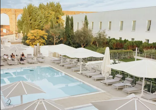 Outdoor pool surrounded by gray reclining chairs and white umbrellas