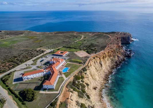 Sky view of white and red hotel building with a large cliff and ocean to the right