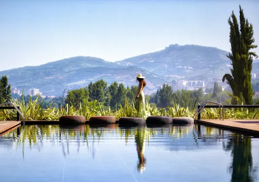 Woman walking along the perimeter of an outdoor pool, looking out towards a large valley