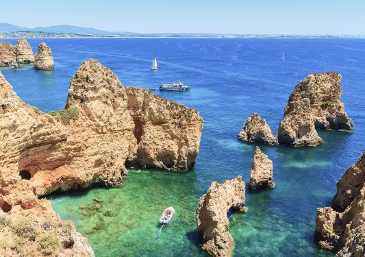 A boat navigating through large cliffs at the edge of the ocean