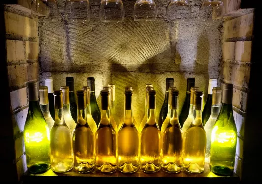 Bottles of wine illuminated by bright lights, with wine glasses hanging from the shelf