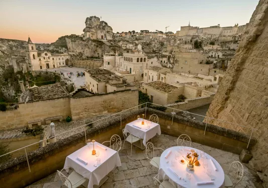 Outdoor balcony on a stone building with white dining tables, overlooking stone ruins and buildings