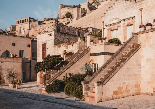 Exterior view of stone hotel building with 2 small staircases, bushes and small trees