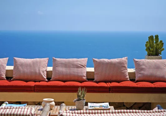 Balcony with cushioned bench with striped pillows, with views of the ocean in the distance