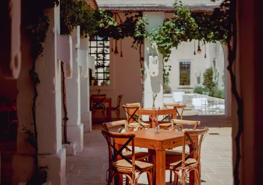 Outdoor patio with wooden tables and chairs, with large, white stone pillars