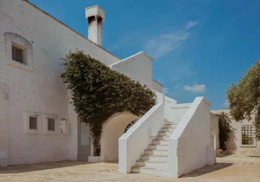 White, stone building with a staircase and bushy tree