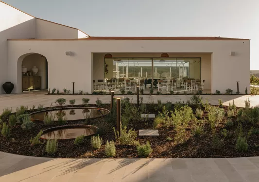 Outdoor view of white building with large windows and an outdoor courtyard and plants