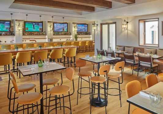 Bar and lounge with tall tables and chairs, with televisions on the wall