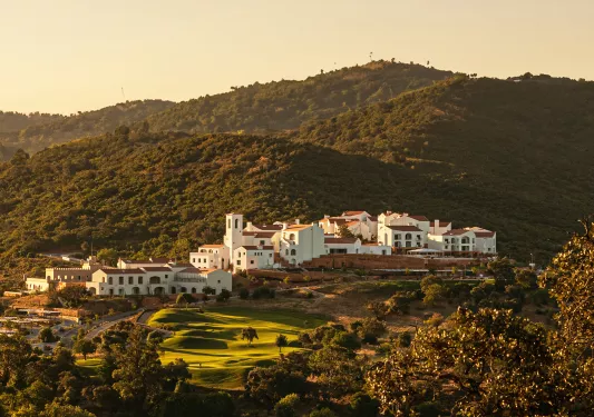 Wide, exterior view of white hotel building complex with tree-covered hills surrounding